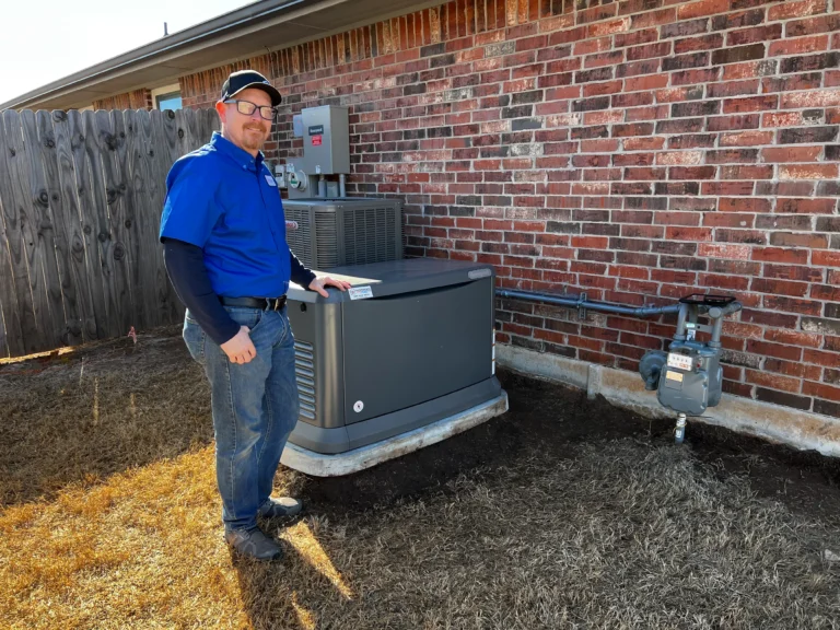 A person in a blue shirt and cap stands next to a large outdoor generator, focusing on home generator repair, beside a brick wall and wooden fence.