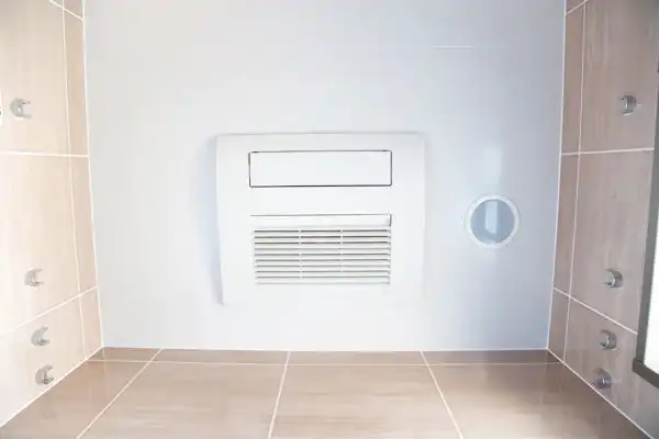 White air vent on a tiled wall with beige and gray tiles, alongside a small circular opening.