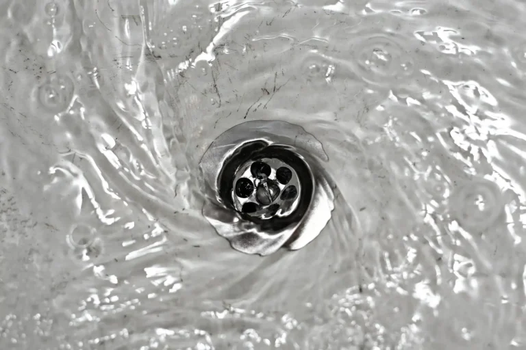 Water swirling down a metal drain creates a mesmerizing whirlpool effect, hinting at the efficient process of drain clearing.