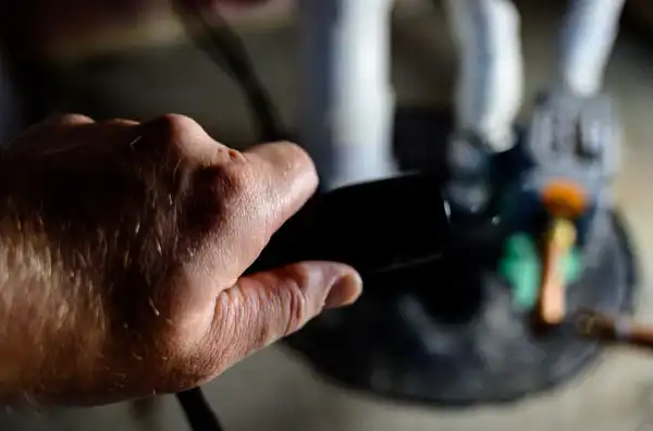 A person holds a black remote control, while a blurred background shows the lower part of figurines standing on a round base.