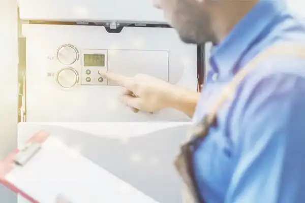 A technician in a blue shirt adjusts the settings on a wall-mounted control panel. He holds a clipboard and turns a dial on the panel.