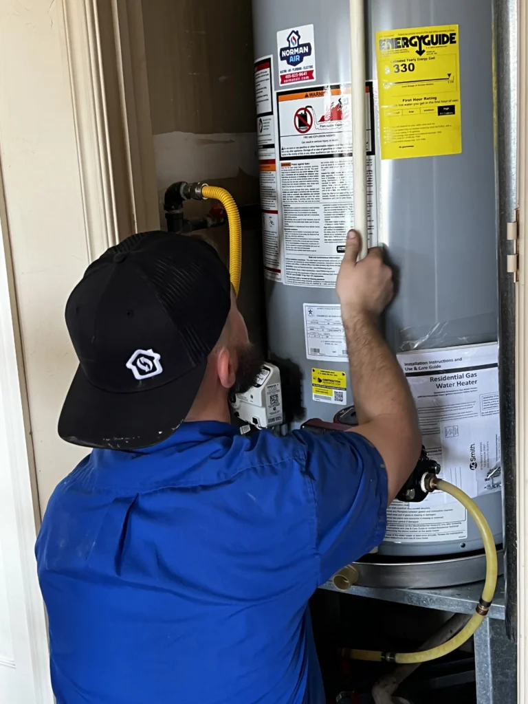 A person in a blue shirt and black cap is carefully fine-tuning the water heater installation in a small enclosed space.